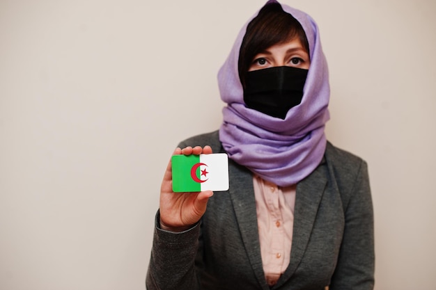 Portret van jonge moslimvrouw die formele kleding draagt, beschermt gezichtsmasker en hijab hoofddoek houdt Algerije vlagkaart tegen geïsoleerde achtergrond Coronavirus landconcept