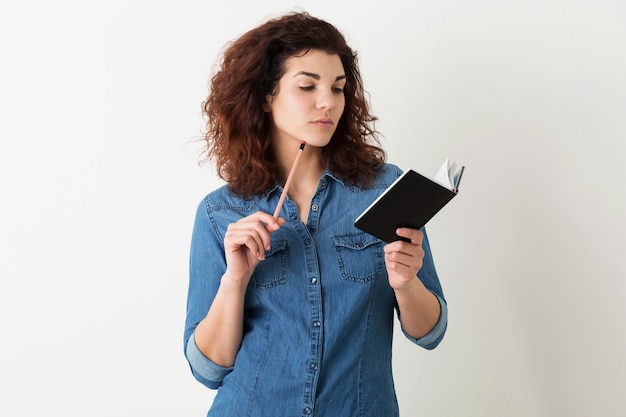 Portret van jonge natuurlijke hipster lachende mooie vrouw met krullend kapsel in denim overhemd poseren met notitieboekje en pen geïsoleerd op witte studio achtergrond, student leren, denken over probleem