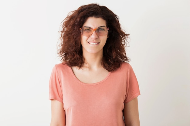 Portret van jonge natuurlijke hipster mooie vrouw close-up met krullend kapsel in roze shirt poseren dragen van een bril geïsoleerd op witte studio achtergrond, grappig gezicht, knipogen