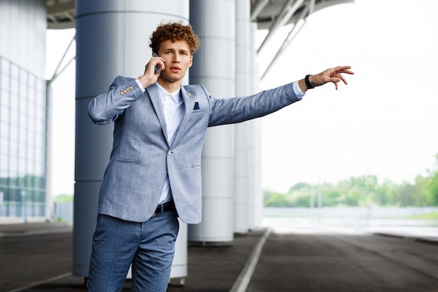 Portret van jonge redhaired zakenman die de auto vangt en op telefoon spreekt