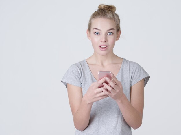 Portret van jonge shoked vrouw met mobiele telefoon in handen - in de studio