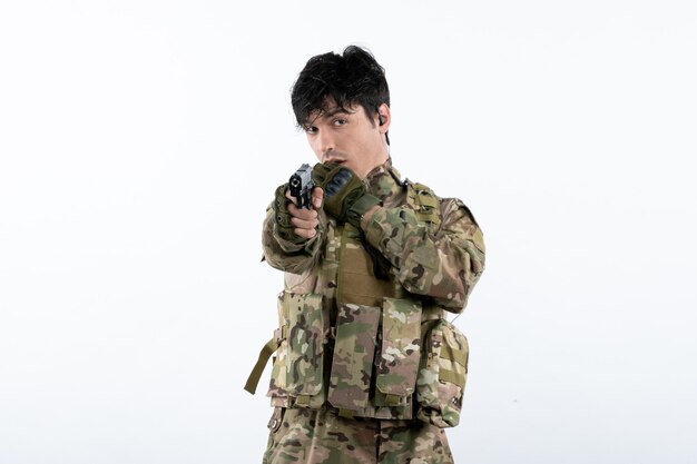 Portret van jonge soldaat in camouflage met pistool op witte muur