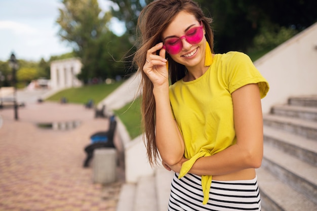 Portret van jonge stijlvolle lachende vrouw met plezier in stadspark, lachende vrolijke stemming, gele top, roze zonnebril, zomer stijl modetrend close-up