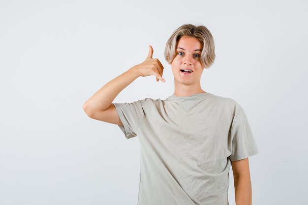 Portret van jonge tienerjongen die telefoongebaar in t-shirt toont en vrolijk vooraanzicht kijkt