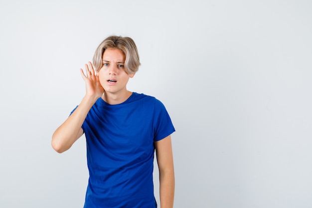 Portret van jonge tienerjongen met hand achter oor in blauw t-shirt en verward vooraanzicht