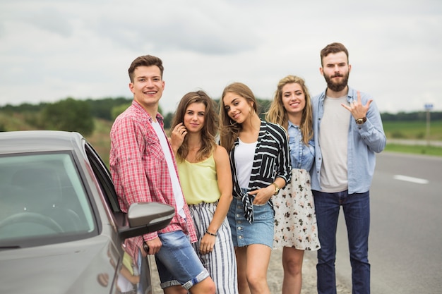 Portret van jonge vrienden die zich dichtbij de auto op weg bevinden