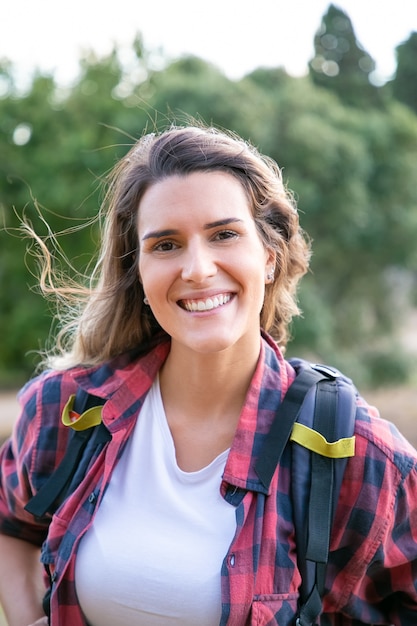 Gratis foto portret van jonge vrolijke dame poseren, glimlachend. mooie blanke vrouw met rugzak, staan en genieten van de natuur. toerisme, avontuur en zomervakantie concept