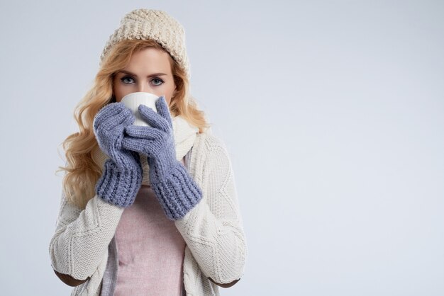 Portret van jonge vrouw die in beanie van hete chocolade genieten tegen copyspace witte achtergrond