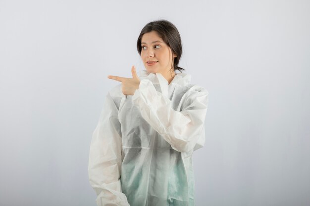 Portret van jonge vrouwelijke arts-wetenschapper in defensieve laboratoriumjas die weg wijst.