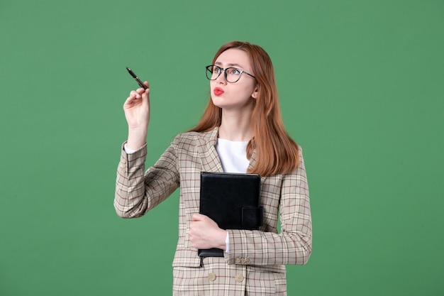 Portret van jonge vrouwelijke leraar in pak met notitieblok op groen