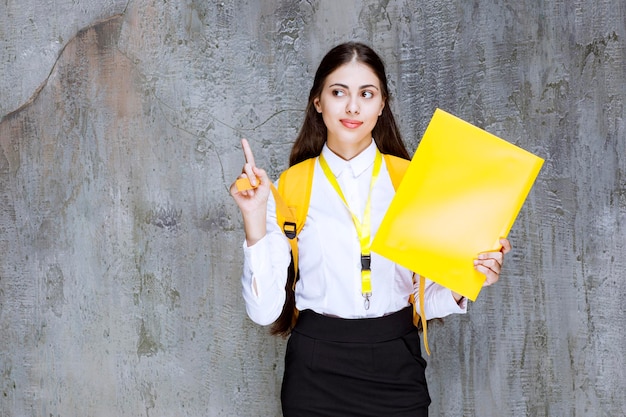 Portret van jonge vrouwelijke student met geel notitieboekje dat zich over grijs bevindt. Hoge kwaliteit foto