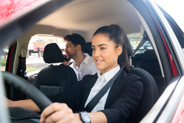 Portret van jonge vrouwelijke taxichauffeur met een zakenmanpassagier op achterbank. Vervoer concept.