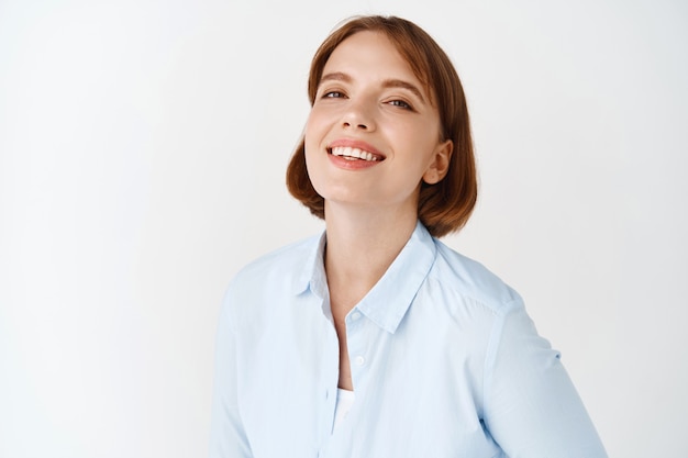 Portret van jonge zakenvrouw glimlachend op witte muur. vrouwelijke ondernemer in kantoorblouse, gemotiveerd en zelfverzekerd