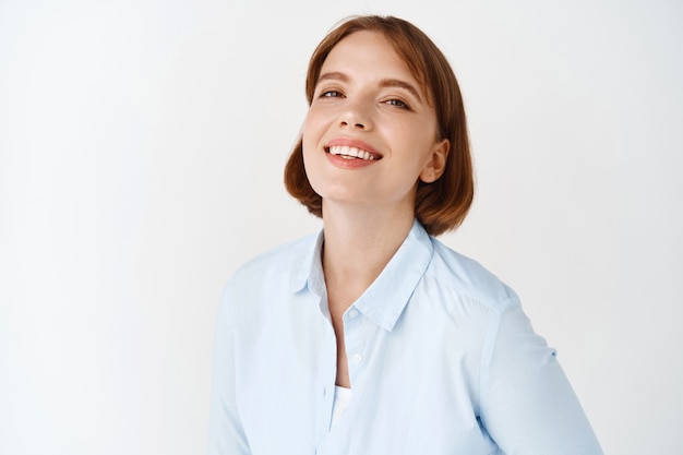 Portret van jonge zakenvrouw glimlachend op witte muur. Vrouwelijke ondernemer in kantoorblouse, gemotiveerd en zelfverzekerd