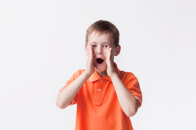 Portret van jongen die met mond open status gilt dichtbij witte muur