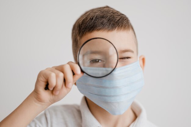 Portret van jongen met medisch masker met een vergrootglas in de klas