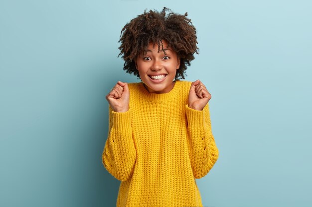 Portret van juichende vrouw met afro poseren in een roze trui