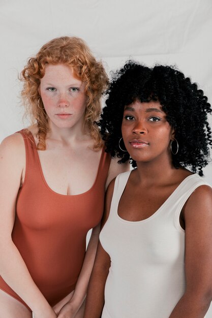 Portret van Kaukasische en Afrikaanse jonge vrouw die camera tegen grijze achtergrond bekijkt