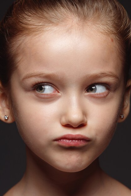 Portret van klein en emotioneel Kaukasisch meisje close-up. Zeer gedetailleerde fotoshoot van een vrouwelijk model met een goed onderhouden huid en een heldere gezichtsuitdrukking. Concept van menselijke emoties. Nadenkend, denkend.