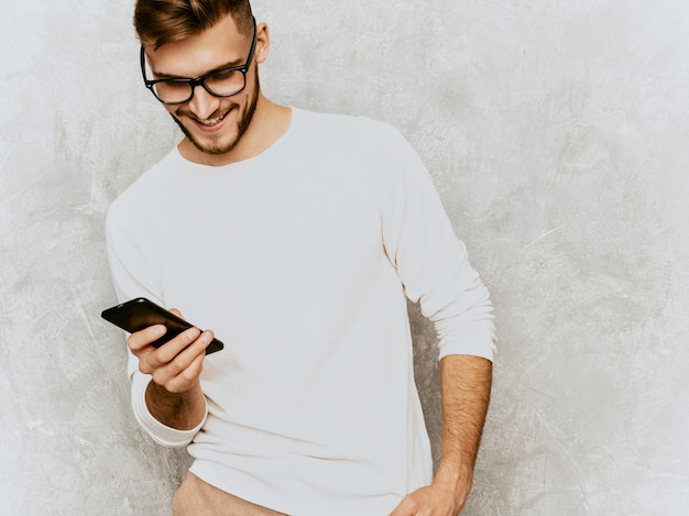 Gratis foto portret van knap glimlachend hipster zakenmanmodel die toevallige de zomer witte kleren dragen. met mobiele telefoon