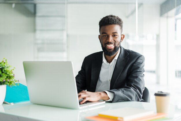 Portret van knappe Afrikaanse zwarte jonge zakenman die op laptop werkt op kantoor