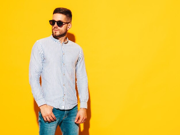 Portret van knappe glimlachende model Sexy stijlvolle man gekleed in shirt en spijkerbroek Fashion hipster man poseren in de buurt van gele muur in studio Summertime