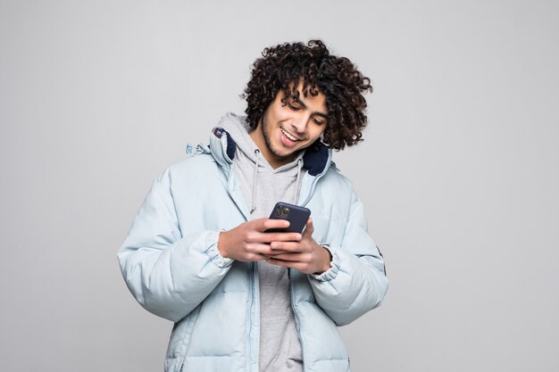 Portret van knappe krullende cellphone van de mensenholding die op witte muur wordt geïsoleerd