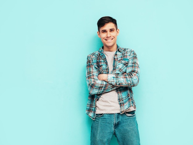 Portret van knappe lachende model Sexy stijlvolle man gekleed in geruit hemd en jeans Fashion hipster man poseren in de buurt van blauw in studio geïsoleerd