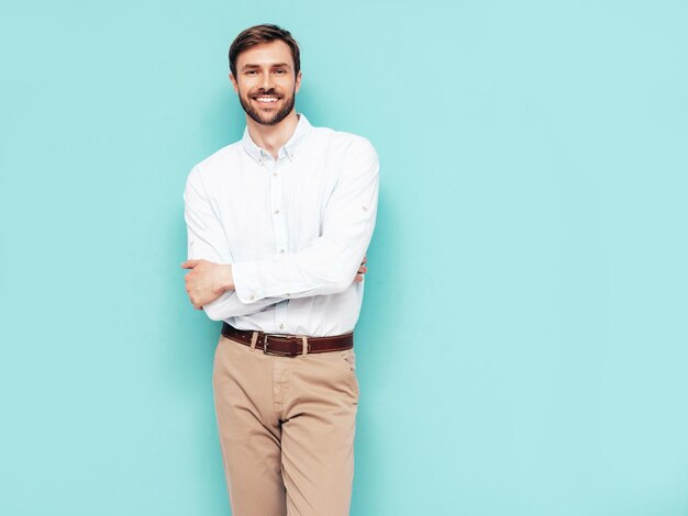 Portret van knappe lachende model Sexy stijlvolle man gekleed in shirt en broek Fashion hipster man poseren in de buurt van blauwe muur in studio geïsoleerd
