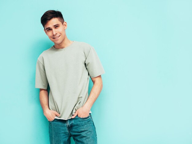 Portret van knappe lachende stijlvolle hipster lamberseksueel model man gekleed in tshirt en jeans mode man geïsoleerd in studio poseren in de buurt van blauwe muur vrolijk en gelukkig