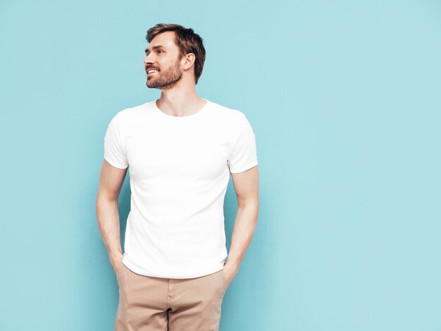 Portret van knappe lachende stijlvolle hipster lamberseksueel model Sexy man gekleed in T-shirt en broek Mode man geïsoleerd op blauwe muur in studio