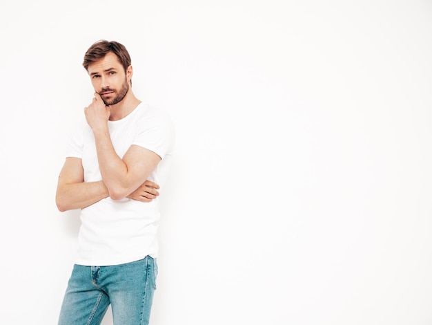 Portret van knappe lachende stijlvolle hipster lamberseksueel model Sexy man gekleed in T-shirt en jeans Fashion man geïsoleerd op een witte muur in studio