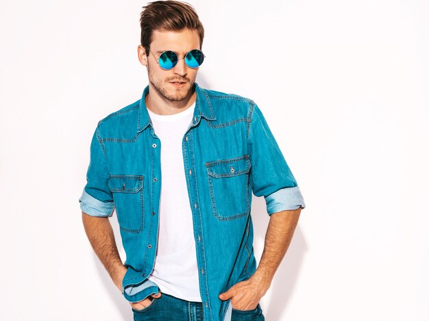 Portret van knappe lachende stijlvolle jonge man model dragen jeans kleding en zonnebril. Mode man