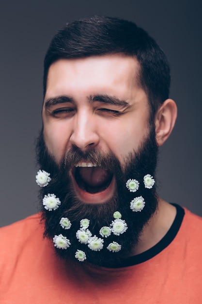 Portret van knappe man met baard van bloemen geïsoleerd op een grijze muur