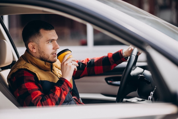 Portret van knappe man zit in auto en koffie drinken