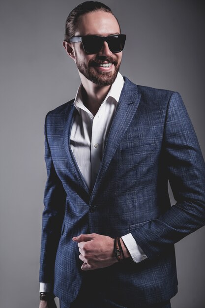 portret van knappe mode stijlvolle hipster zakenman model gekleed in elegant blauw pak in zonnebril die zich voordeed op grijs