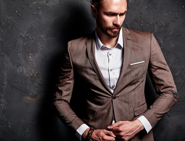 portret van knappe mode stijlvolle hipster zakenman model gekleed in elegant bruin pak in de buurt van donkere muur