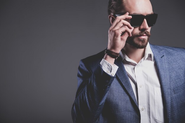 portret van knappe mode stijlvolle hipster zakenman model gekleed in elegante blauwe pak poseren op grijs