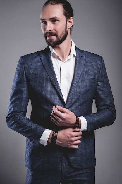 portret van knappe mode stijlvolle hipster zakenman model gekleed in elegante blauwe pak poseren op grijs