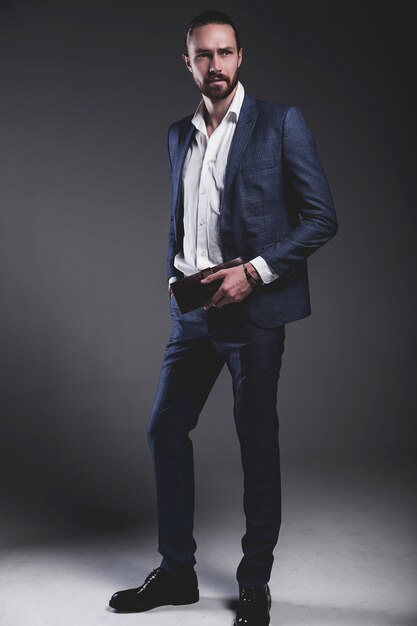 portret van knappe mode stijlvolle hipster zakenman model gekleed in elegante blauwe pak poseren op grijs