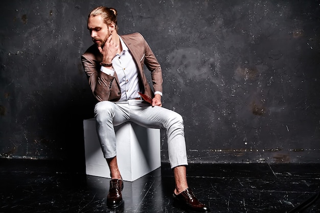 portret van knappe mode stijlvolle hipster zakenman model gekleed in elegante bruine pak zitten in de buurt van donker in de studio