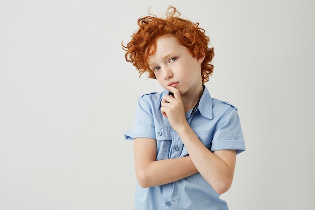 Portret van knappe roodharige jongen met sproeten hand in hand in de buurt van mond, op zoek