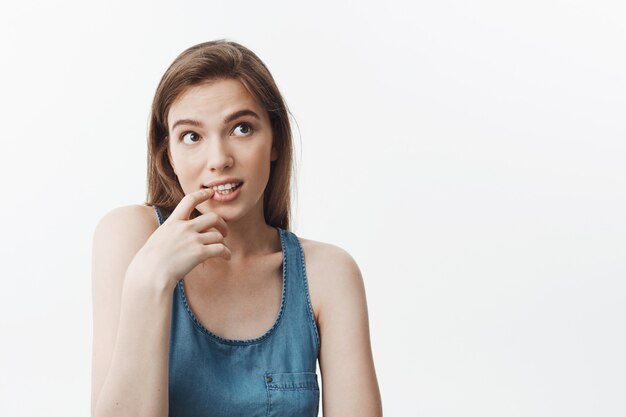 Portret van knappe sexy Europese brunette student meisje met lang haar glimlachen, opzij kijken met dromerige uitdrukking, vinger in de buurt van mond houden