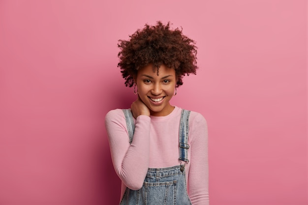 Portret van knappe tedere vrouw houdt de hand op de nek, lacht zachtjes, heeft een verlegen uitdrukking tijdens gesprekken met vriend, verheugt zich op een mooi moment in het leven, ontvangt een hartverwarmend compliment