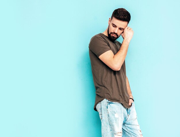 Portret van knappe zelfverzekerde stijlvolle hipster lamberseksueel model man gekleed in tshirt en jeans mode man geïsoleerd op blauwe muur in studio