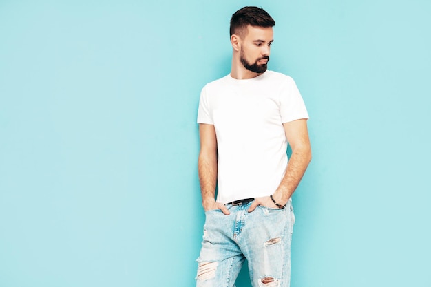 Portret van knappe zelfverzekerde stijlvolle hipster lamberseksueel model man gekleed in witte tshirt en jeans mode man geïsoleerd op blauwe muur in studio
