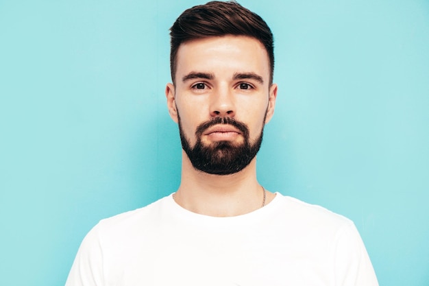 Portret van knappe zelfverzekerde stijlvolle hipster lamberseksueel model man gekleed in witte tshirt en jeans mode man geïsoleerd op blauwe muur in studio