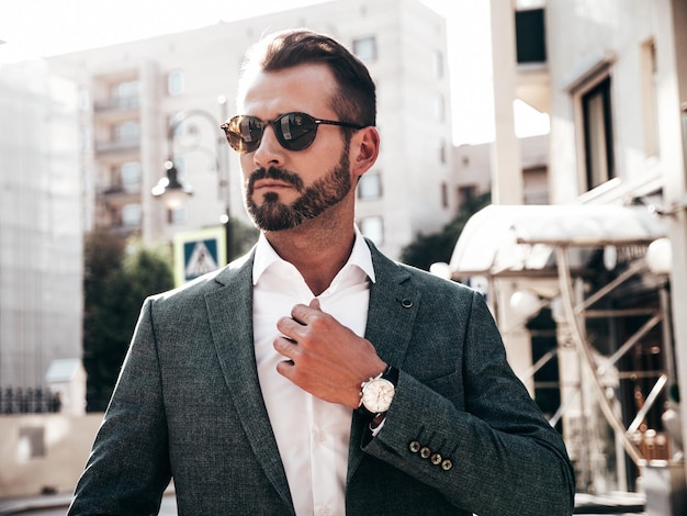 Portret van knappe zelfverzekerde stijlvolle hipster lamberseksueel model moderne man gekleed in elegante pak mode man poseren op de straat achtergrond in Europa stad bij zonsondergang In zonnebril