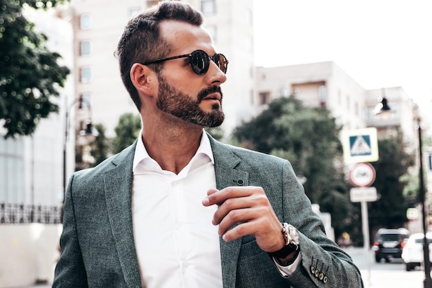 Portret van knappe zelfverzekerde stijlvolle hipster lamberseksueel model moderne man gekleed in elegante pak mode man poseren op de straat achtergrond in Europa stad bij zonsondergang In zonnebril