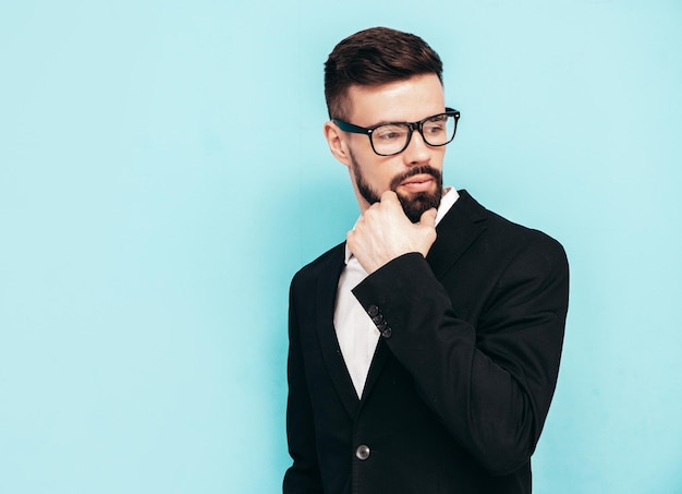 Portret van knappe zelfverzekerde stijlvolle hipster lamberseksueel model Sexy moderne man gekleed in elegant zwart pak Mode man poseren in studio in de buurt van blauwe muur